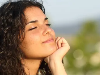 Stock photograph of a model: a smiling woman with curly hair rests her chin on her hand outdoors