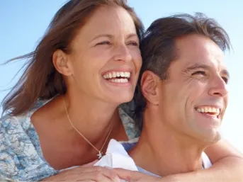 Stock photograph of models: a smiling couple embrace outdoors under a bright sky