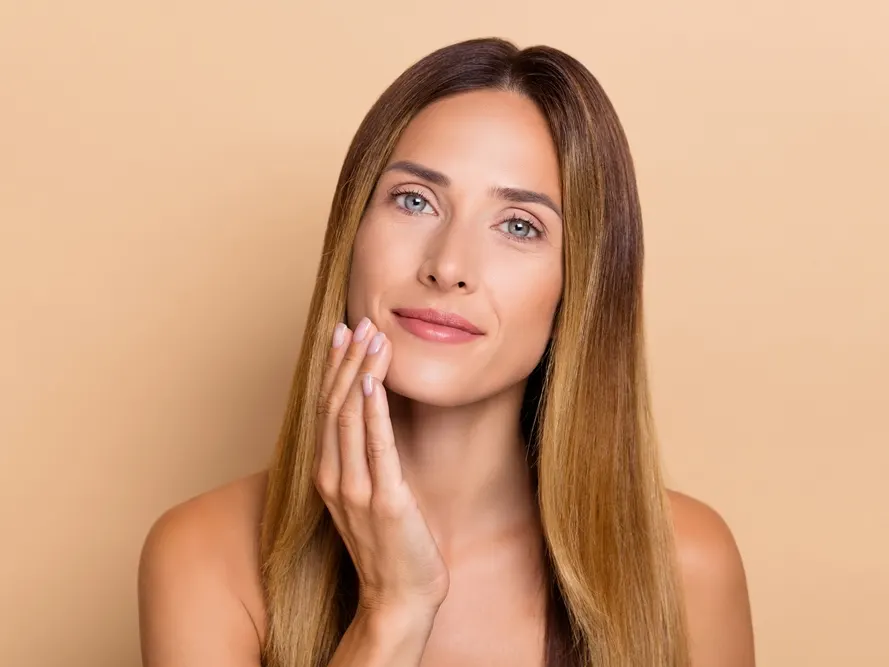 Stock photograph of a model: a woman with long hair rests her fingertips on her cheek against a peach background