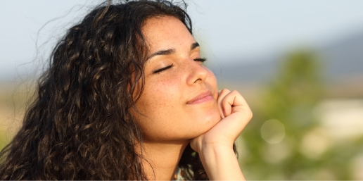 Stock photograph of a model: a smiling woman with curly hair rests her chin on her hand outdoors