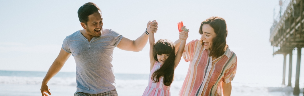 Stock photograph of models: a family of four on a beach, the parents lifting a child between them, a pier behind them
