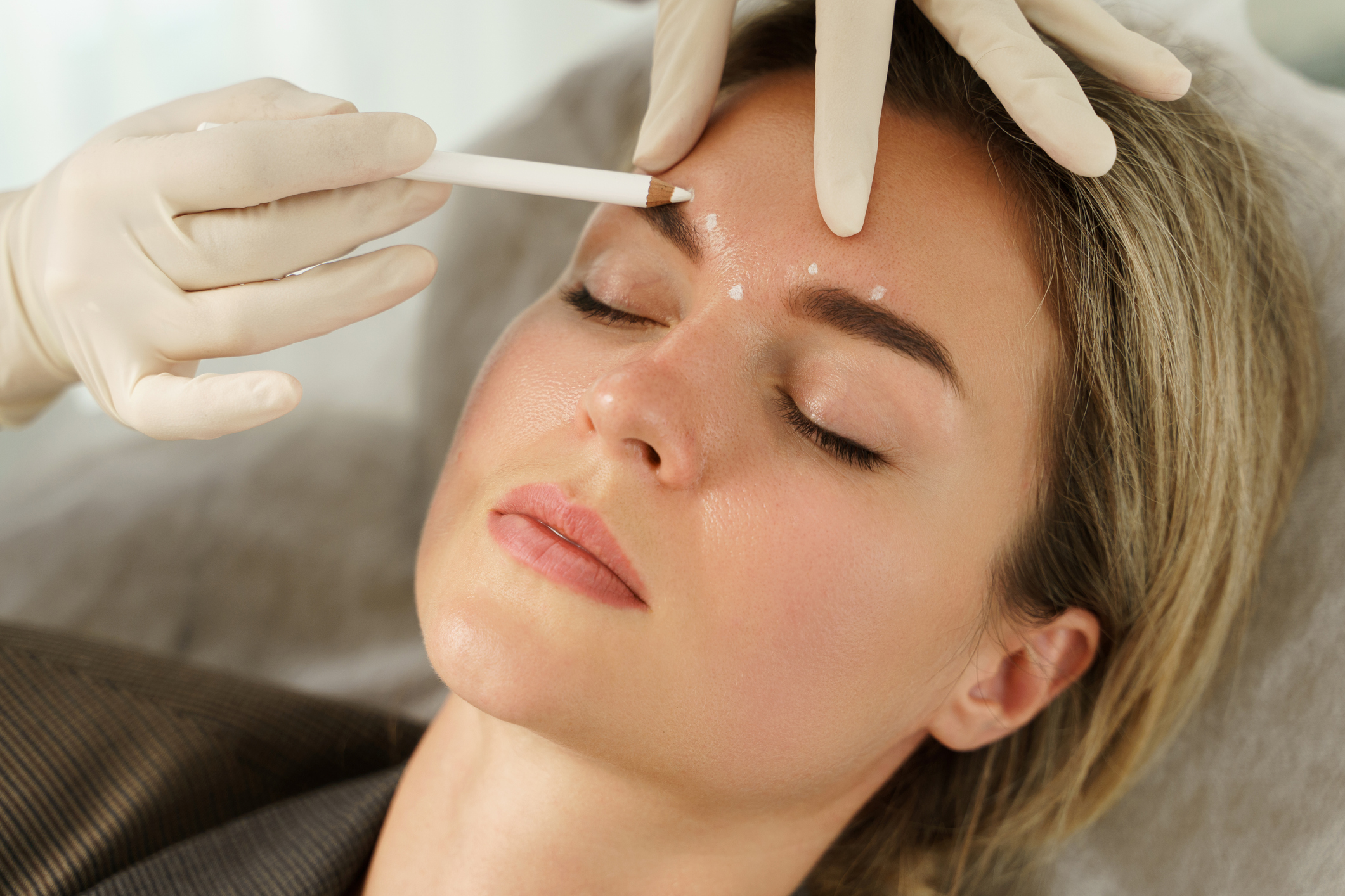 Stock photograph of a model: a woman lies back with her eyes closed while a gloved hand marks points on her forehead